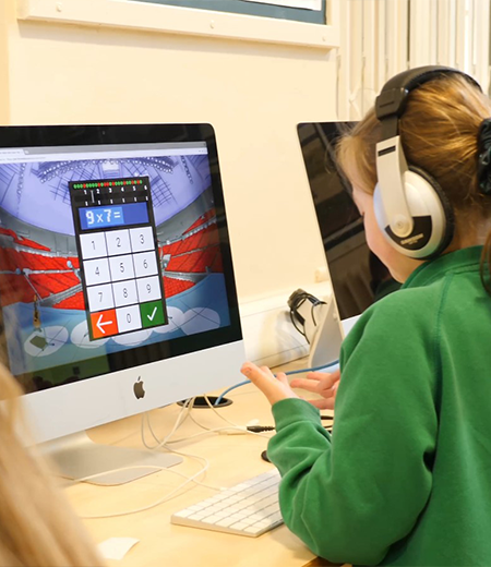 A young girl wearing headphones using the calculator on an iMac