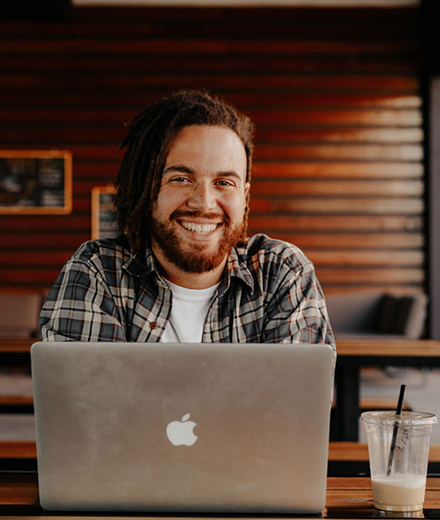 A smiling man with dreadlocks sat with a macbook