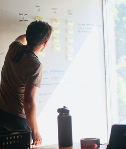 A man in a t-shirt working with sticky notes on a whiteboard